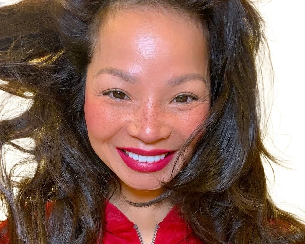 Melinda Bui smiling in red, wearing a vivid pink-red lip color